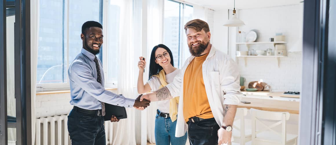 Realtor shaking hands with smiling couple in new condo  kitchen.