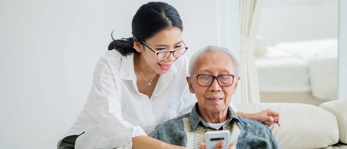 A young Asian woman assisting her father with a phone, possibly related to technology or communication assistance.