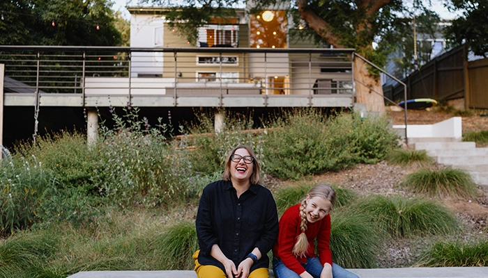 Mom and daughter sitting on short wall laughing.
