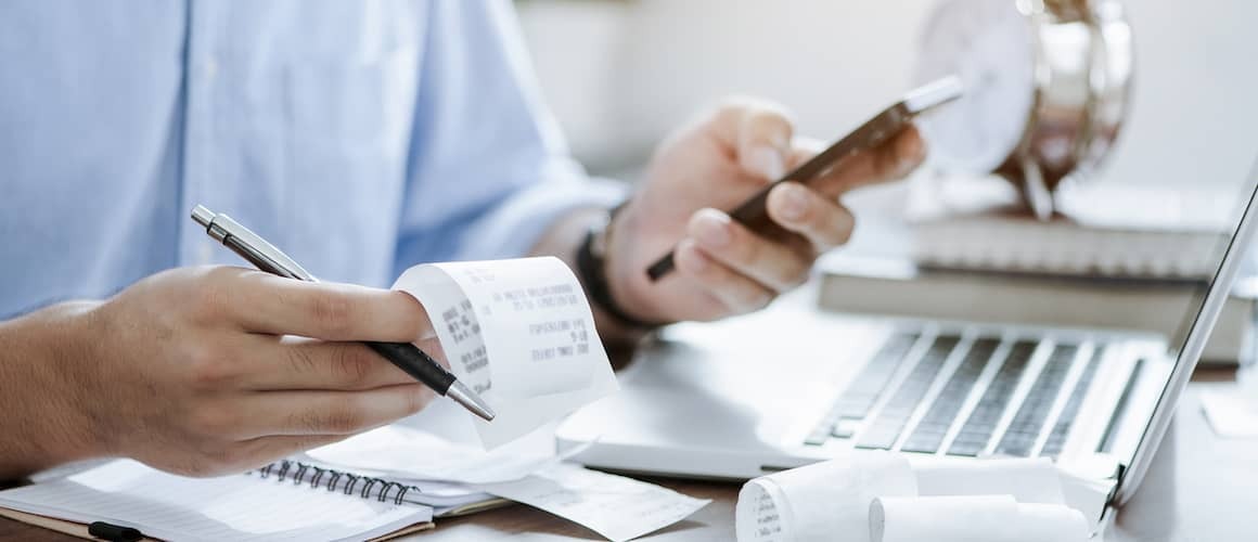 Man balancing checkbook with pile of receipts.