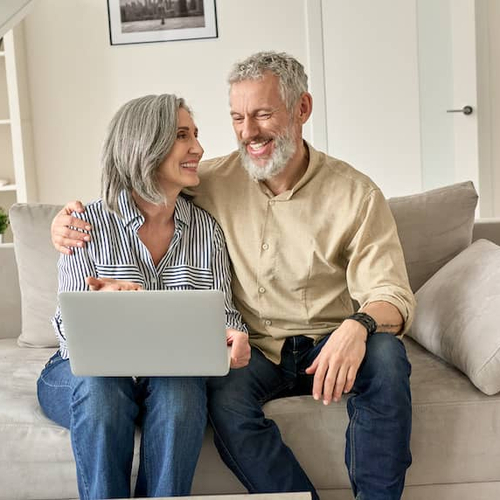 A couple on a couch looking at a laptop, possibly researching or managing their mortgage online.
