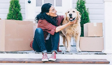 Woman sitting on her porch with her golden retriever surrounded by boxes.