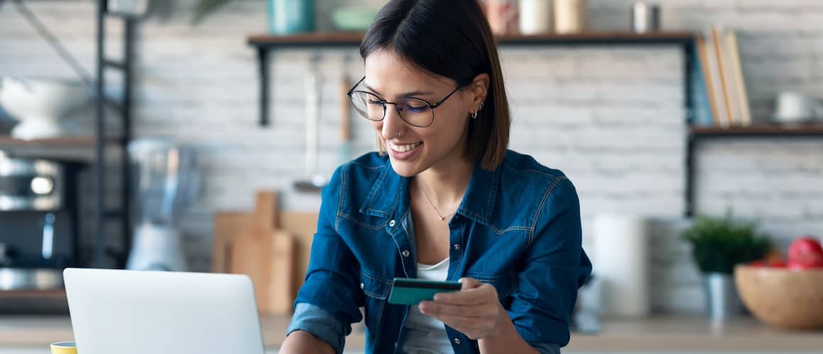 Woman on laptop using credit card in kitchen.