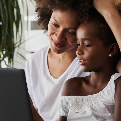 A woman and child sitting on a couch, engrossed in a laptop.