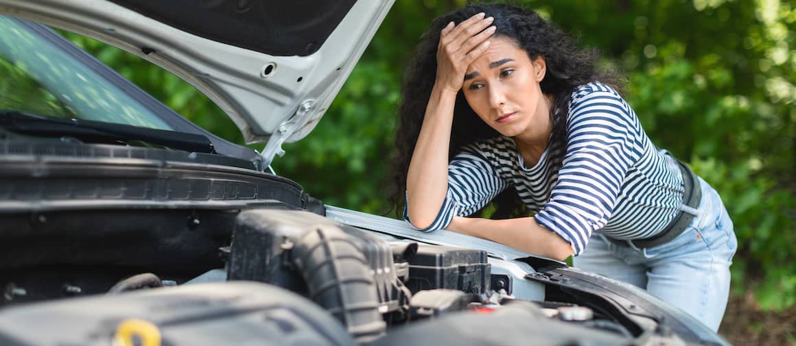 Woman looking under hood of broken-down car.