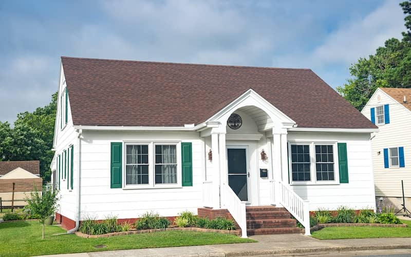 Small white coastal cottage with green shutters and modest yard. 