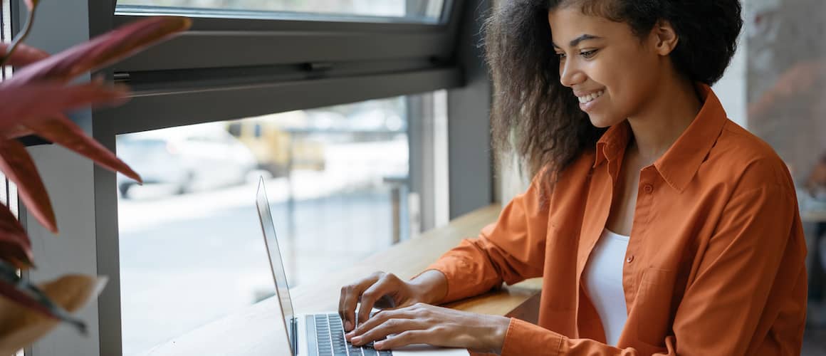 woman in orange searching on laptop in cafe