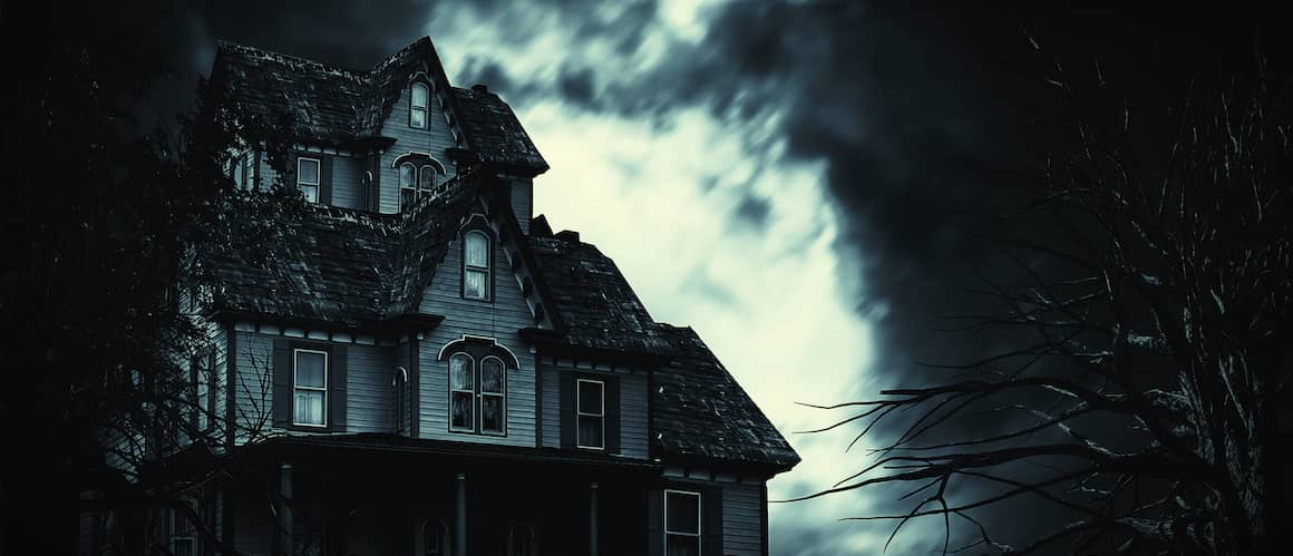 Dark and spooky Victorian house with dark sky and bare tree branches.