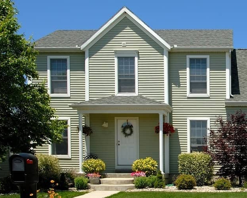 A green two-story house by a tree.