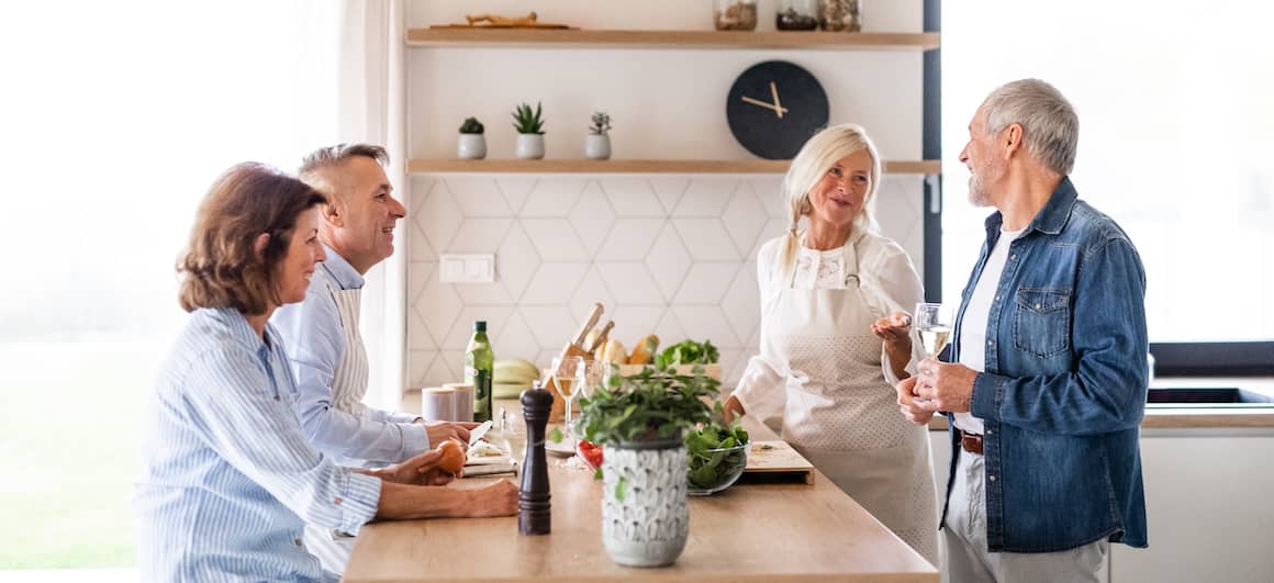 Two couples in a kitchen discussing something.