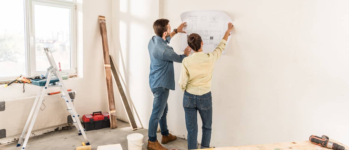 A couple examining blueprints against a wall, potentially involved in home renovation or construction planning.