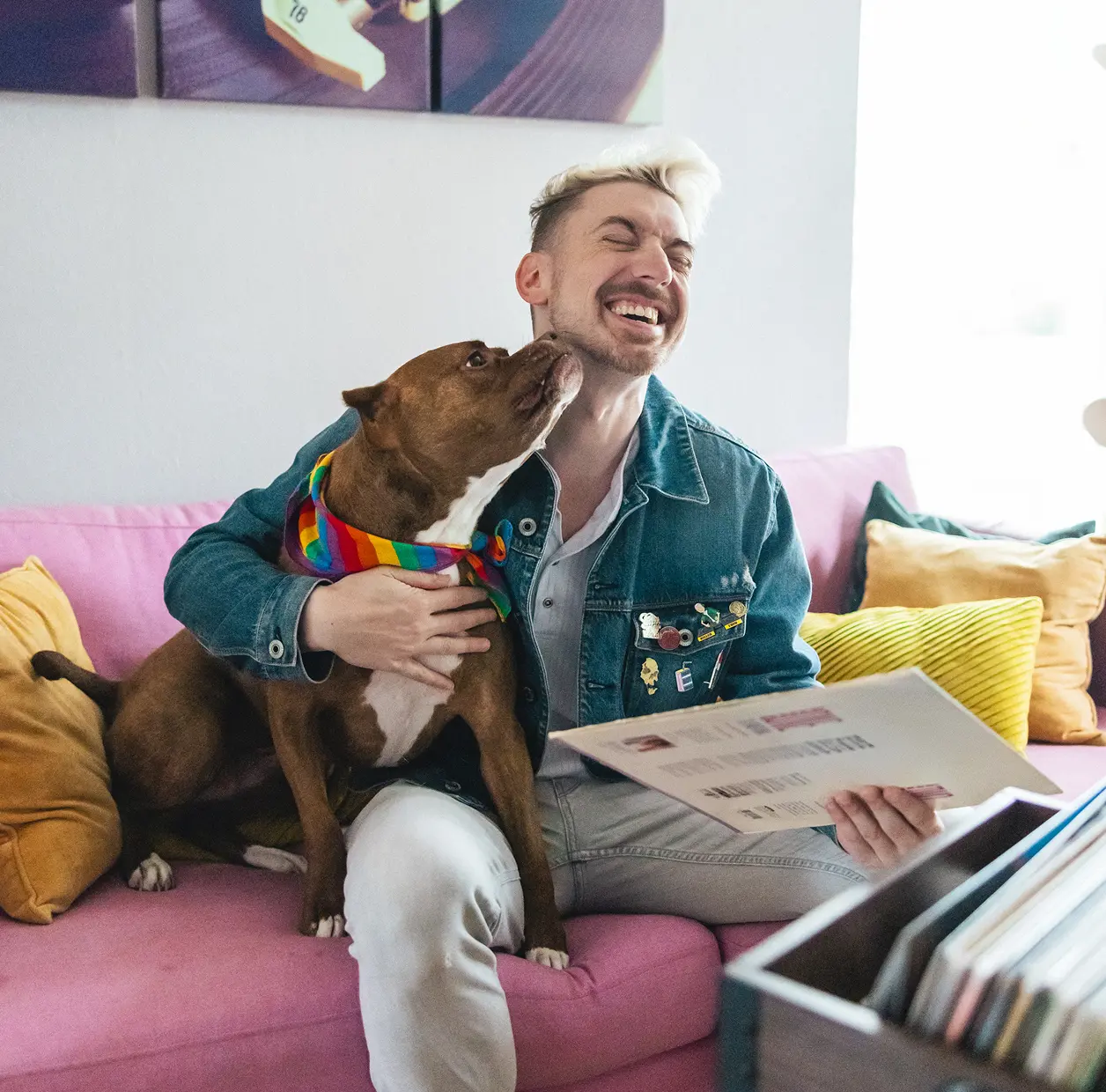 A man sits on his couch smiling and laughing with his dog