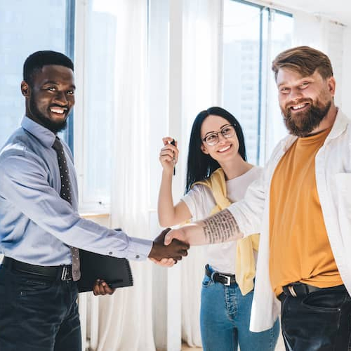 Realtor shaking hands with smiling couple in new condo kitchen.