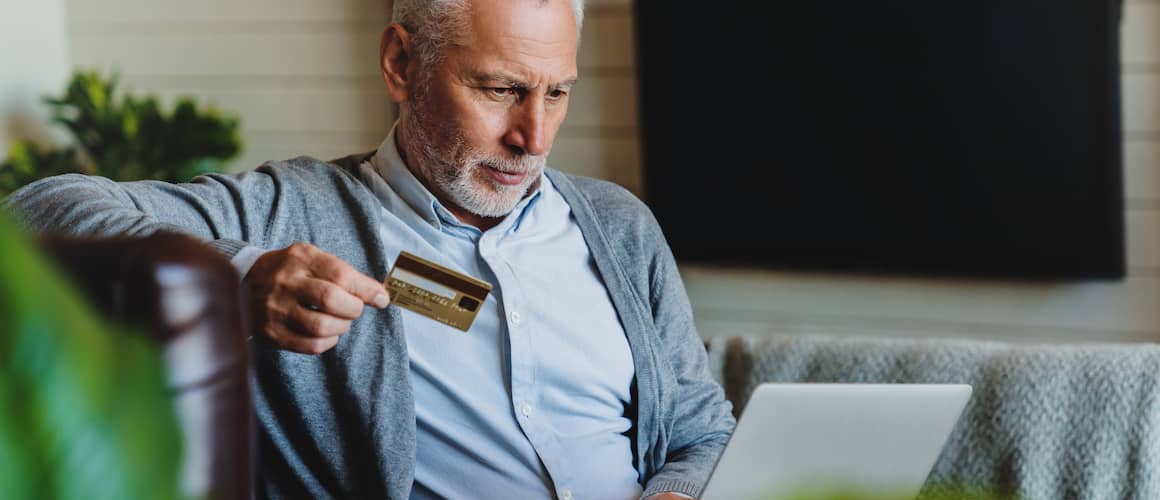 Image of man looking down, using credit card as revolving debt on computer.