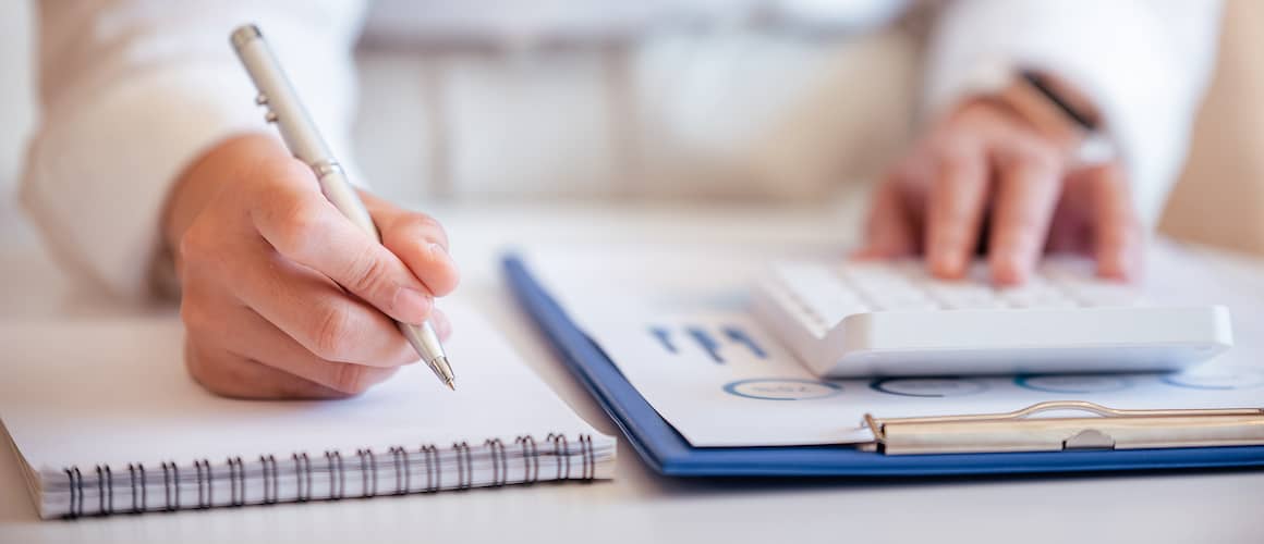 Hands pressing a calculator and writing on a notepad, signifying financial calculations or planning.