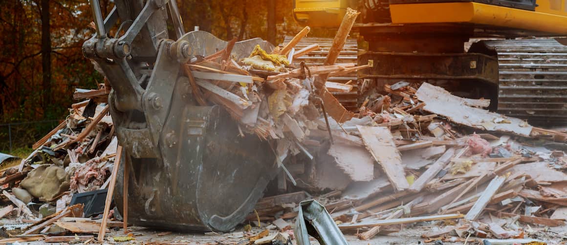 Closeup of a backhoe removing rubble from the site of a demolished house.