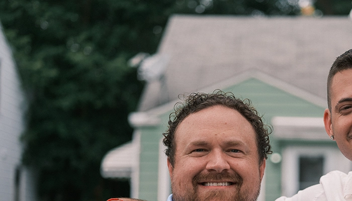 Man in white shirt with arm around man in blue shirt smiling.