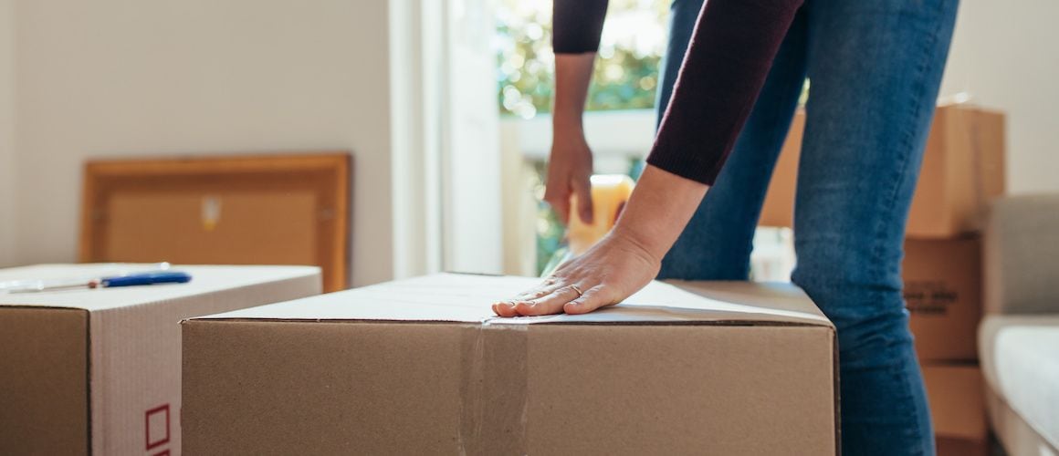 A woman sealing a box with tape, possibly indicating the process of moving or packing belongings for a new home.