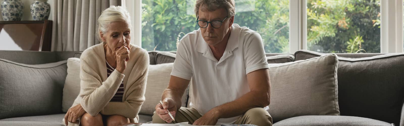 An elderly couple sitting on couch possibly calculating taxes or investments.