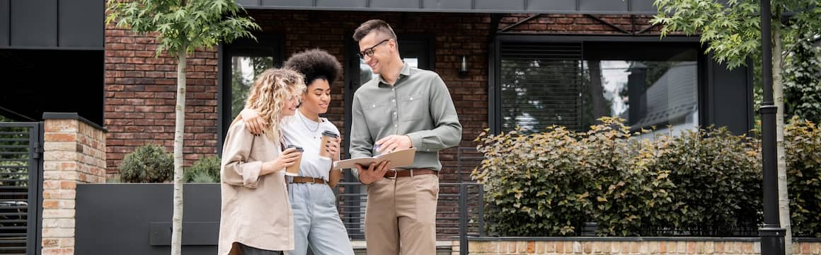 Couple looking over documents for house  with Realtor in front of property for sale.