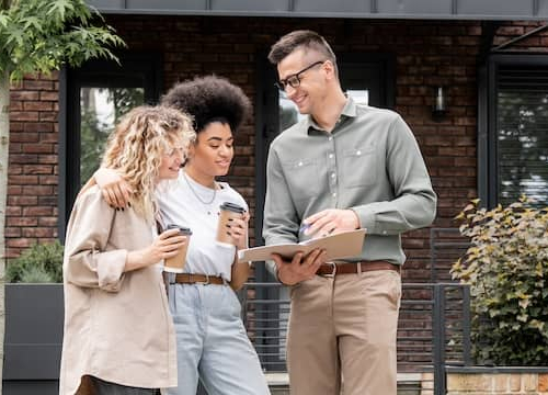 Couple looking over documents for house  with Realtor in front of property for sale.