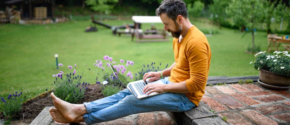 A man sitting on the backyard steps with his laptop, engrossed in his work outdoors.