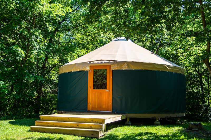 Green yurt in a wooded area.