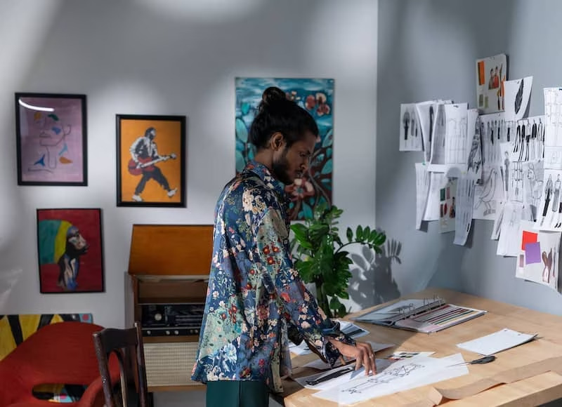 Young man in a garage converted into an art studio with a desk and papers.