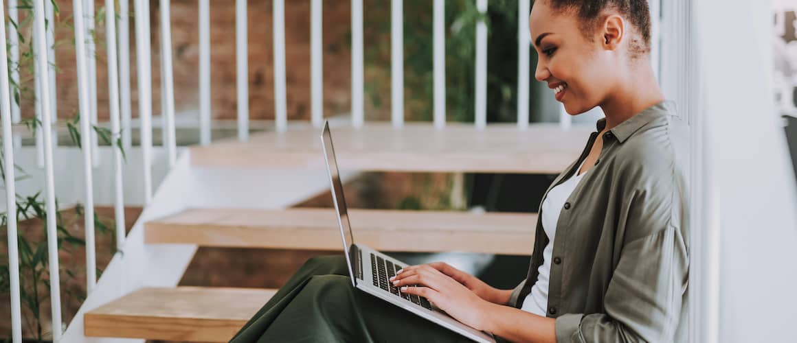 Black woman on patio on laptop smiling, showing a woman on a patio, potentially working on a laptop and smiling.