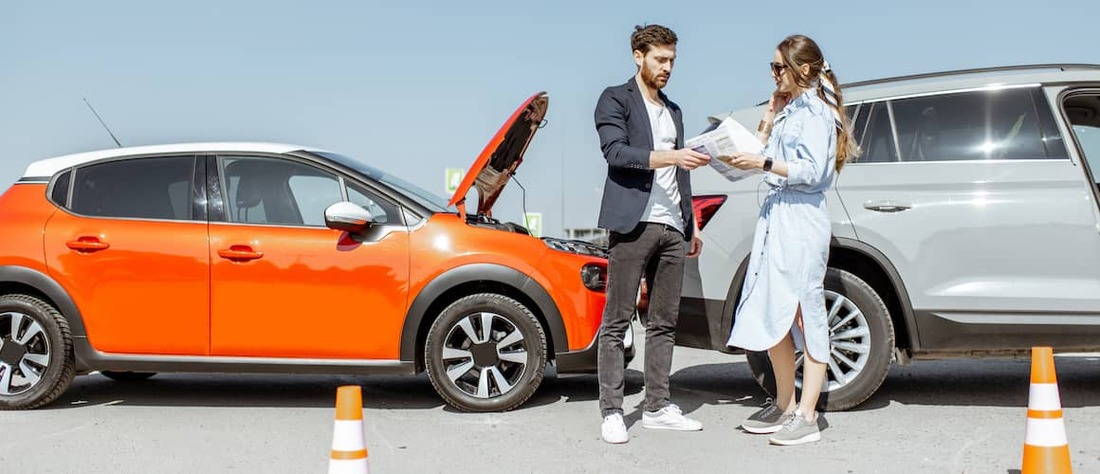 Two people outside their cars exchanging insurance after a minor accident.