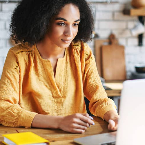 A woman using a laptop in the kitchen, indicating remote work or online activities in a home environment.