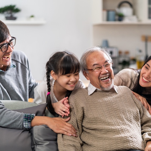 Multigenerational Asian family smiling and socializing in their living room.