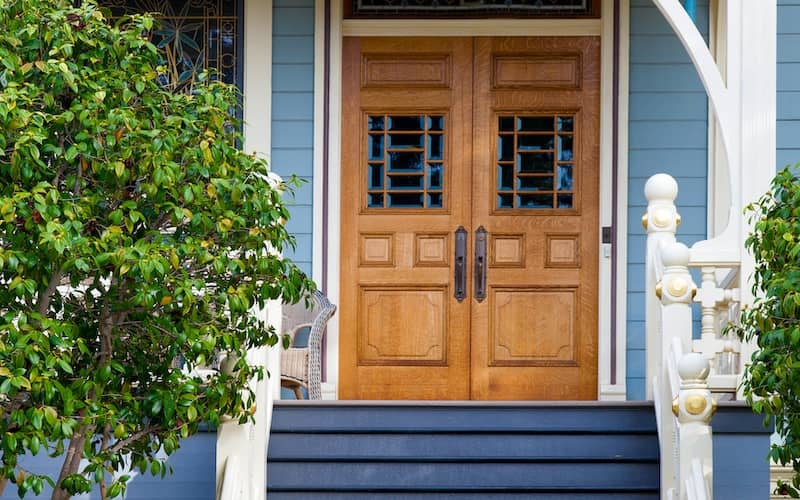 Home with light blue siding, light wooden front door and steps painted dark blue. 