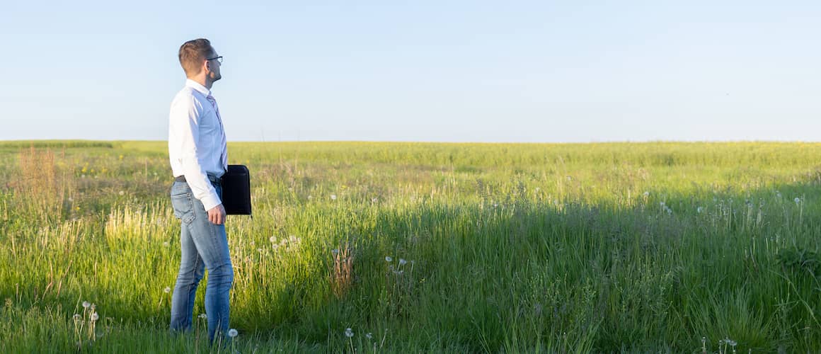 Man holding portfolio standing in field with tall grass.