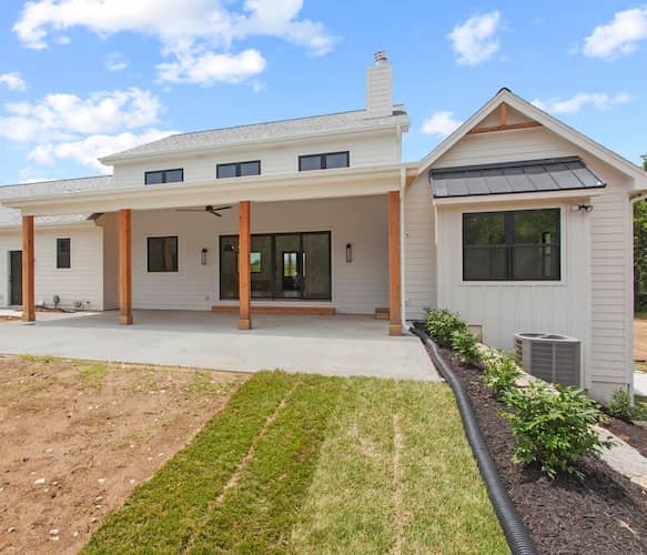 New construction farmhouse style home in last phase of build with white siding and covered porch.