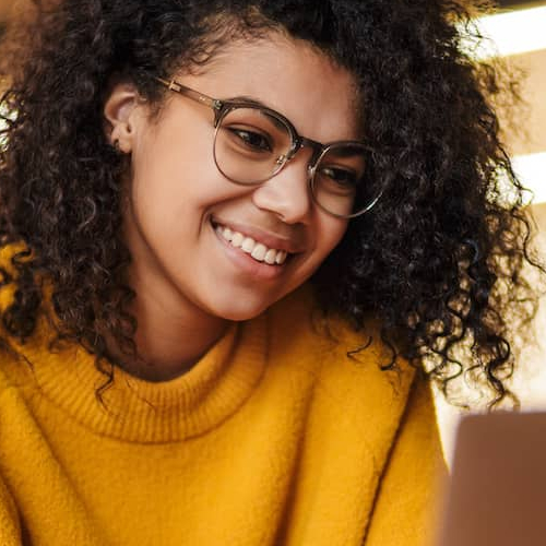 A woman in a sweater looking at a laptop, possibly working or engaging in online activities.