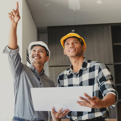 Photograph of contractors holding large house blueprints at a newly built construction site, related to construction or real estate development.