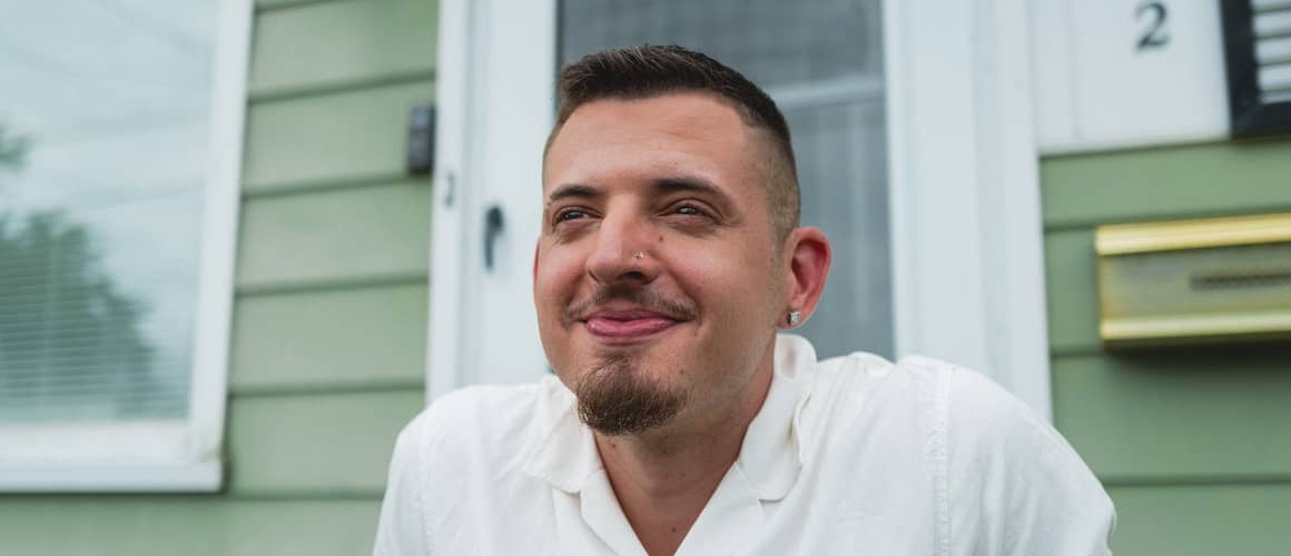 Man smiling, sitting on porch of home.