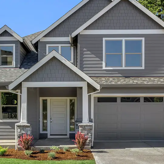 A modern home with gray paint and white trim, with simple landscaping and shrubs in the front yard