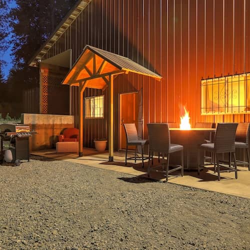 Barndominium in forest with lit firepit in front. 