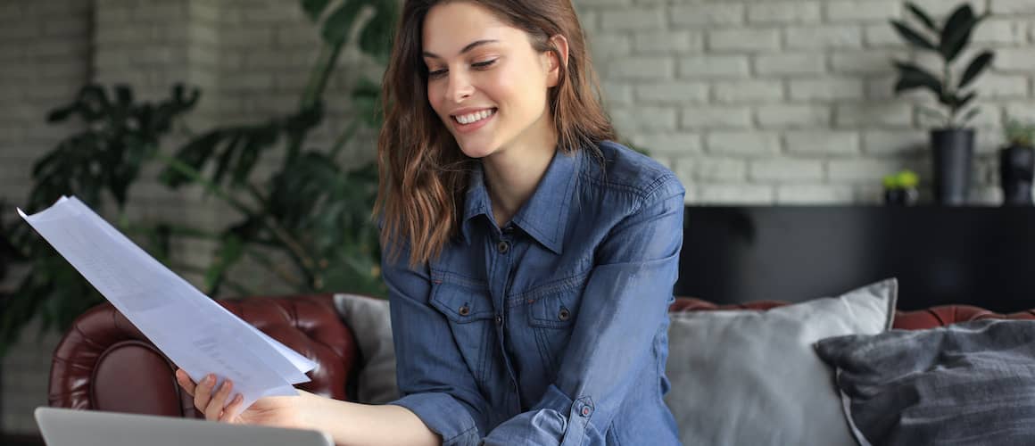 Woman with brown hair reading some papers while sitting on the couch.