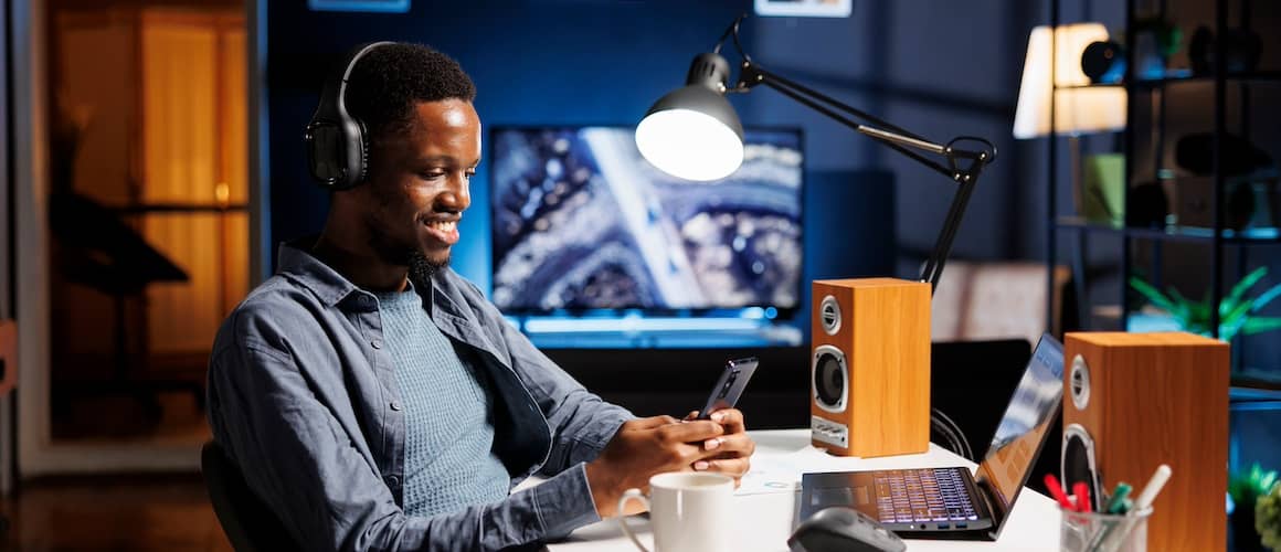 Young man sitting at his desk and smiling while using his smart phone.