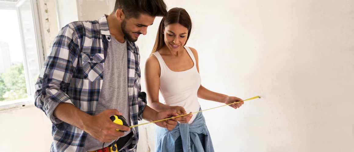 A couple holding a measuring tape possible going to renovate their house.