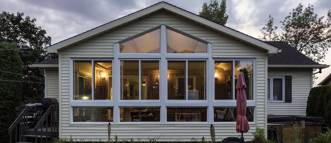 An evening view of a house with many windows gives a peak of the inside of the home with all its lights on.