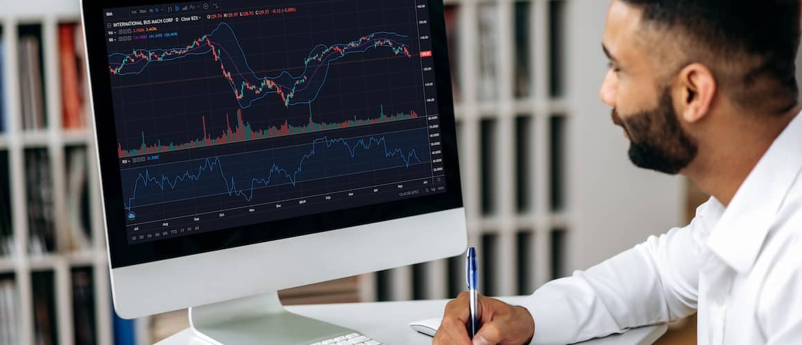 Man taking notes while analyzing various financial charts.