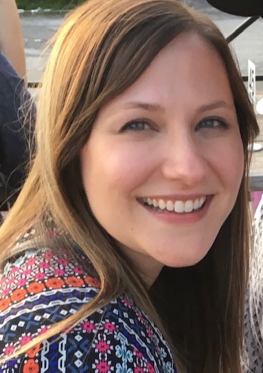 Headshot of a woman smiling over her shoulder at the camera as she sits outside on a sunny day.