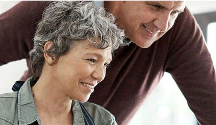 Two people looking at a computer screen with one standing behind the other in a bright indoor setting.