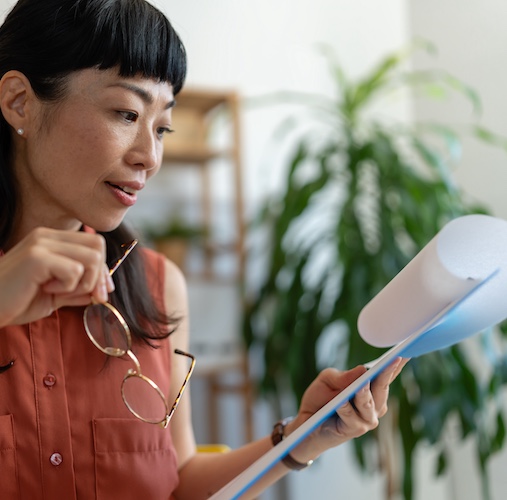 Woman reviewing multiple pages of loan agreement with eye glasses in her hand.