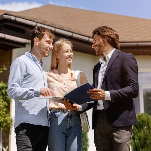 Real estate agent standing with couple in front of a house looking at documents in a folder.