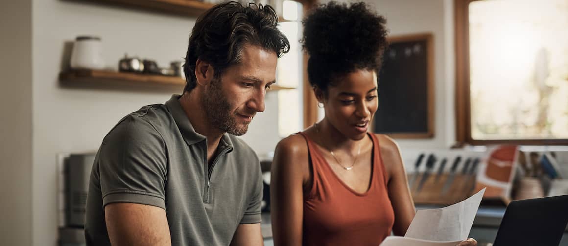 Couple looking at bills and working on laptop, going over finances in a kitchen.